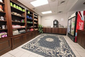 A coffee station with shelves stocked with various items, a Coca-Cola refrigerator, and a patterned rug on the floor.