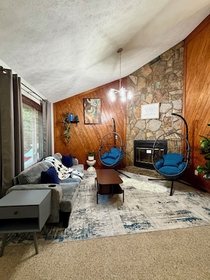 Sala de estar com parede de pedra, cadeira suspensa, sofá e mesa de centro.