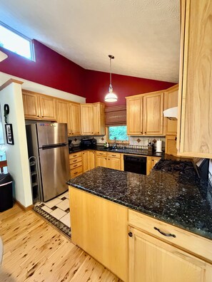 Cocina con armarios de madera, refrigerador de acero inoxidable, encimera de granito y lámpara colgante.