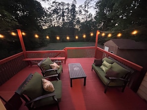 Terraza exterior con barandal rojo, mobiliario verde y luces colgantes.