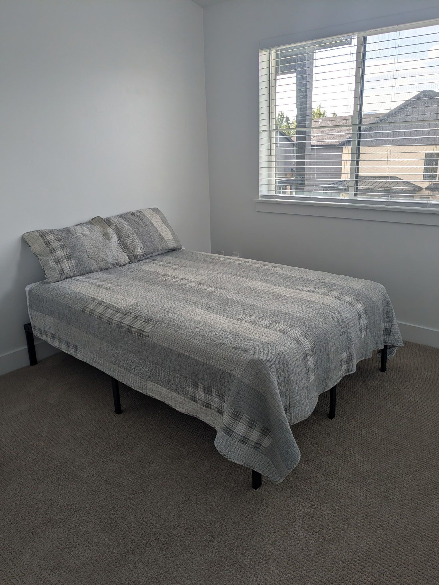 Een slaapkamer met een enkel bed, een raam met zonwering en een vloerbedekking.