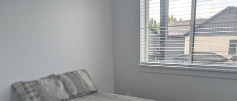 Un dormitorio con una cama individual, una ventana con persianas y suelo cubierto de alfombra.