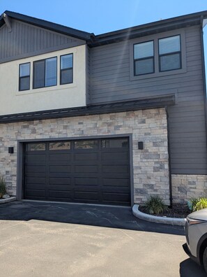 A two-story house with a garage, stone facade, and a clear sky. - 2-bedroom townhome in Midway (Midway)