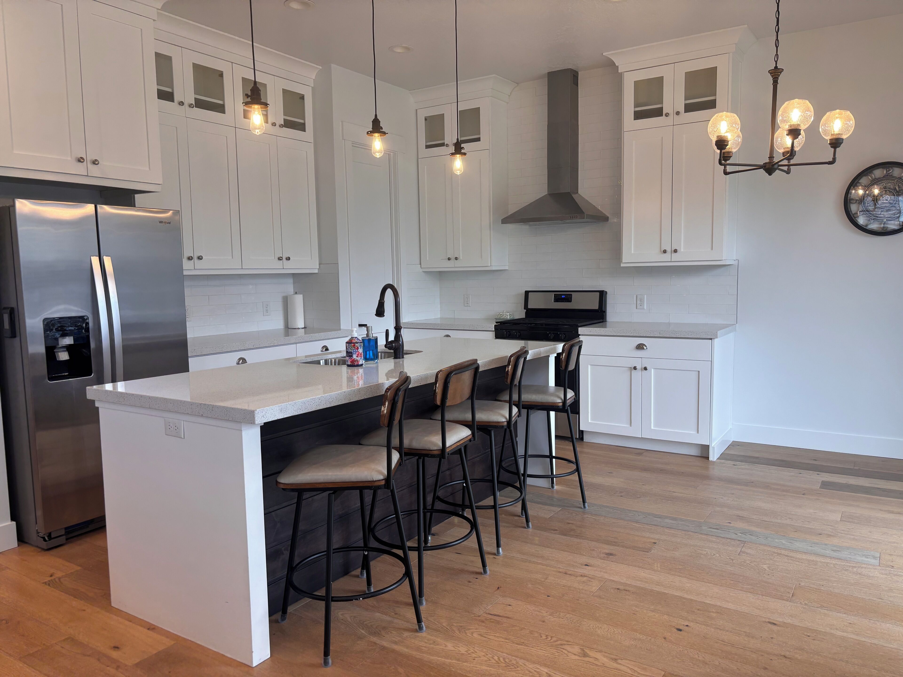 A modern kitchen with white cabinetry, a stainless steel refrigerator, a central island with bar stools, and pendant lighting.