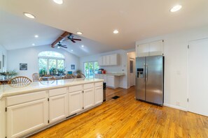 Una cocina amplia con suelo de madera, armarios blancos, una isla grande y un refrigerador de acero inoxidable.