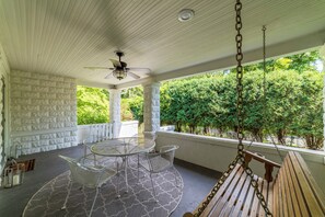 Un patio techado con mesa y sillas, un ventilador de techo y vista a follaje.