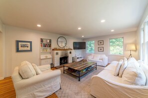 A living room with a fireplace, white sofas, a coffee table, and a bookshelf. - 3-acre farmhouse retreat, pool & hot tub in Saywer (Sawyer)