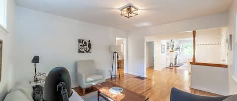A modern living room with a sofa, a coffee table, and a lamp. There is a hallway leading to a kitchen area.