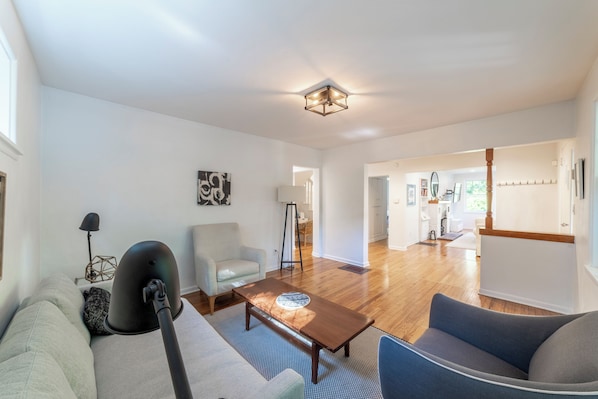 Una sala de estar moderna con un sofá, una mesa de centro y una lámpara. Se ve un pasillo que conduce a una zona de cocina.