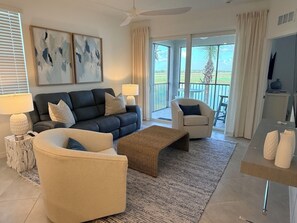 A modern living room with a sofa, armchairs, a coffee table, and a view of the outdoors through large windows.