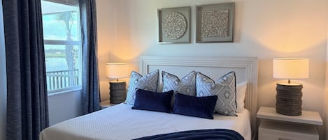 A bedroom with a bed, two bedside tables with lamps, a ceiling fan, and artwork on the wall.