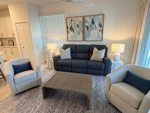 A living room with a dark sofa, two armchairs, a coffee table, and a ceiling fan.