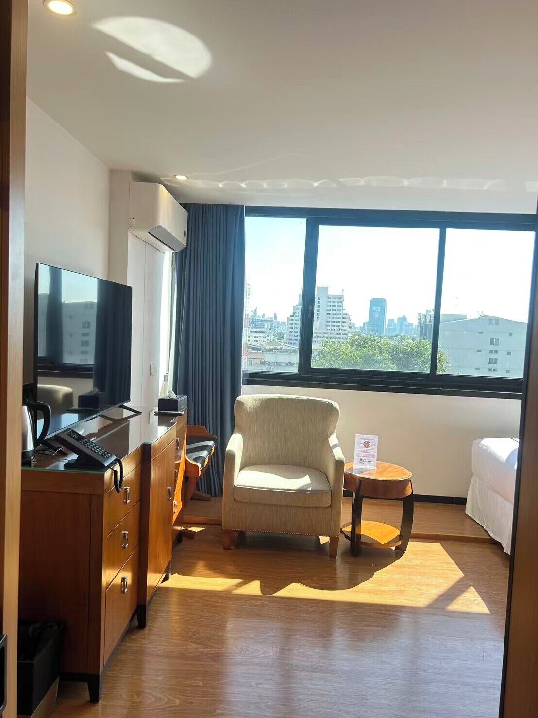 Une chambre d’hôtel équipée d’un lit, d’une télévision, d’un bureau avec un ordinateur, d’une chaise et offrant une vue sur la ville grâce à de grandes fenêtres.