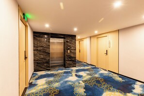 Un pasillo con un ascensor, una puerta con el símbolo del número y una alfombra estampada.