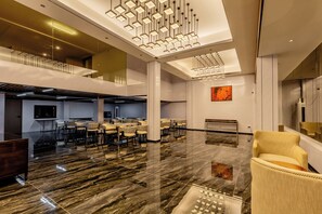 A spacious lobby with a high ceiling, modern lighting fixtures, and a seating area with chairs and tables.