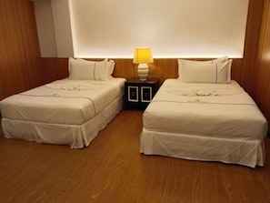 Habitación de hotel con dos camas, una mesita de noche con lámpara y paneles de madera en las paredes.