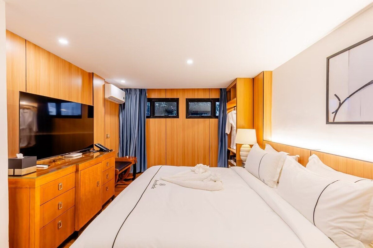 A hotel room with a large bed, a TV, wooden furniture, and a window with curtains.
