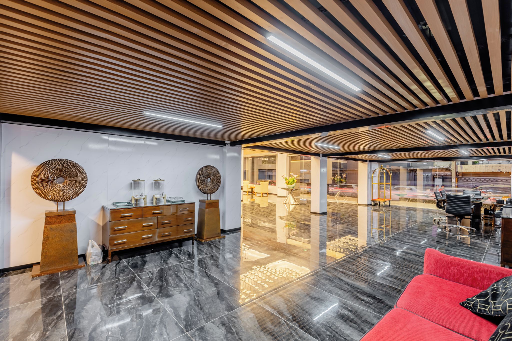 A modern lobby with a marble floor, wooden ceiling, and a red sofa.