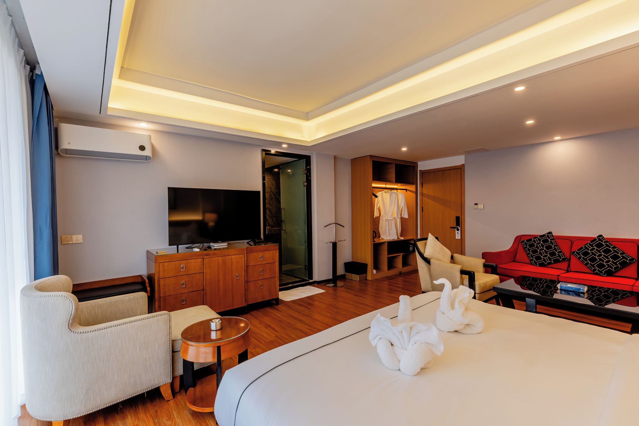 A hotel room with a bed, a TV, a wardrobe, a red sofa, and a small table.
