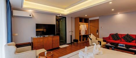 A hotel room with a bed, a TV, a wardrobe, a red sofa, and a small table.