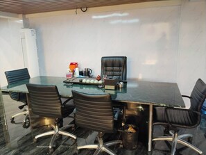 A conference room with a glass table, four chairs, a black leather chair, and a white wall with a vent. - Aesthetic Hotel (Krung Thep Maha Nakhon)