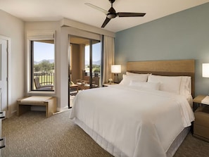 Ein Hotelzimmer mit einem großen Bett, einem Deckenventilator, einem Fenster mit Aussicht, einem Nachttisch und einer Bank am Fenster.