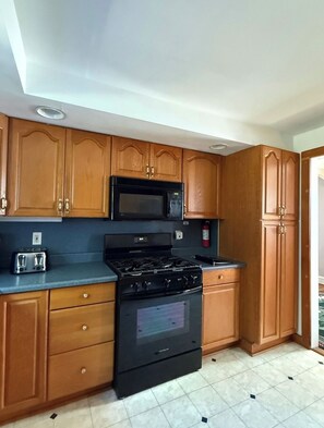 A kitchen with wooden cabinets, a microwave, a stove, and a toaster. - Webster’s Place — A charming Bar Harbor home (Bar Harbor)