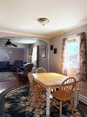 A dining area with a wooden table and chairs, a ceiling fan, and a window with curtains. - Webster’s Place — A charming Bar Harbor home (Bar Harbor)