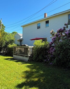 A residential house with a wooden deck, a red umbrella, and purple flowering bushes. - Webster’s Place — A charming Bar Harbor home (Bar Harbor)