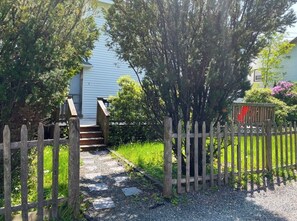 A wooden gate leading to a gravel path, surrounded by greenery and a house with a porch. - Webster’s Place — A charming Bar Harbor home (Bar Harbor)