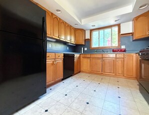 A kitchen with wooden cabinets, a black refrigerator, a dishwasher, and a window providing natural light. - Webster’s Place — A charming Bar Harbor home (Bar Harbor)