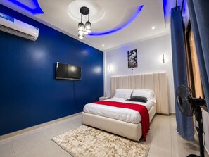 Un dormitorio moderno con cama, televisor de pantalla plana, ventilador de techo y aire acondicionado.