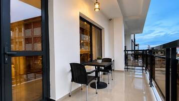 A modern balcony with a glass door, a dining table with chairs, and a hanging light fixture.