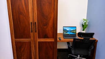Ein Zimmer mit einem Holzschrank, einem Schreibtisch mit Laptop, einem Stuhl und einem kleinen Topfpflanzen.