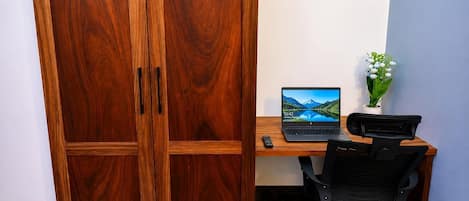 Una habitación con un armario de madera, un escritorio con una computadora portátil, una silla y una planta pequeña en maceta.