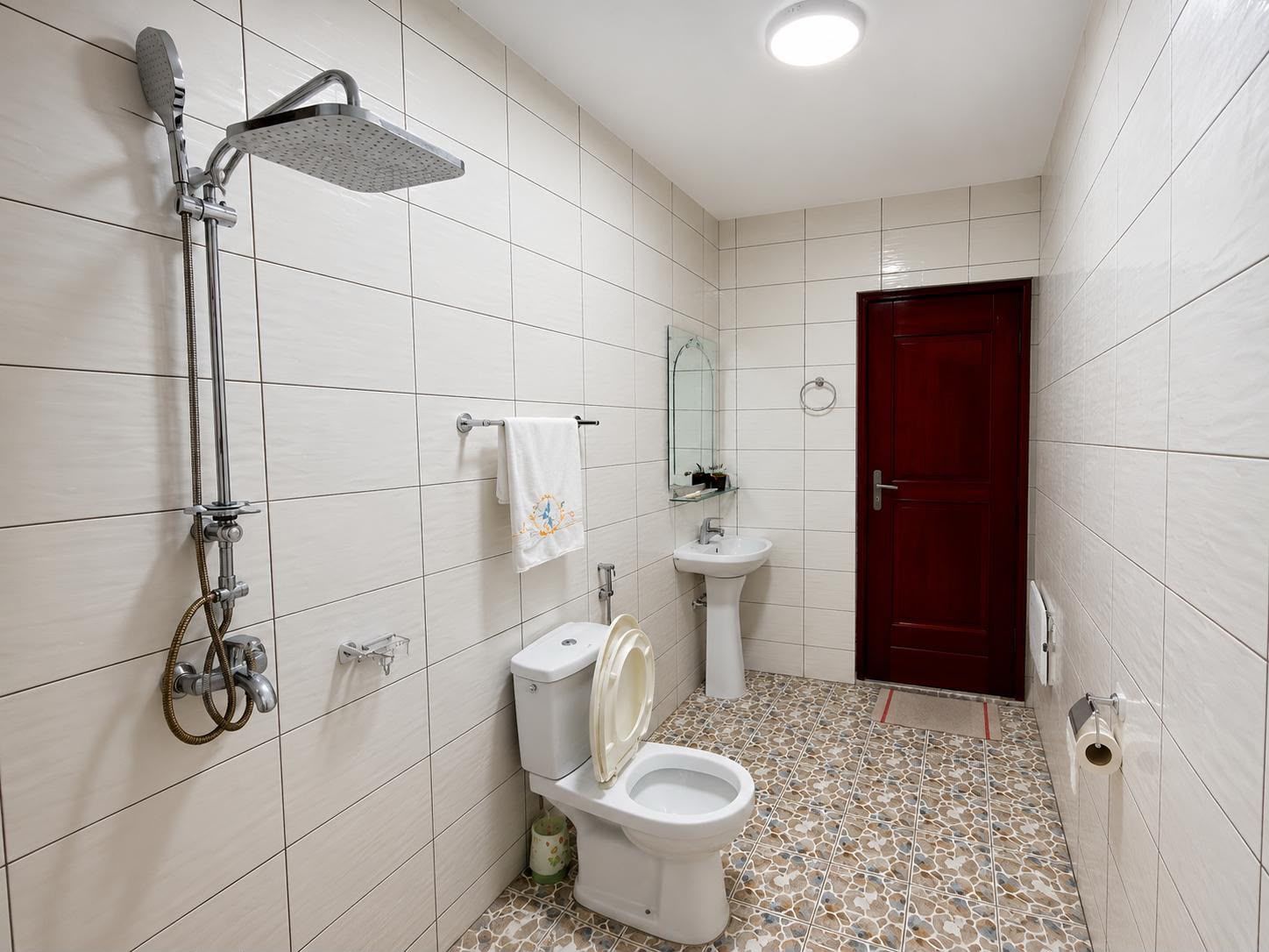 Une salle de bain avec une douche, des toilettes, un lavabo et une porte rouge.