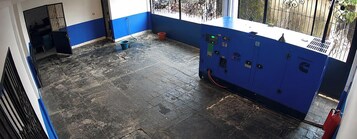 Una habitación con pared azul, un panel de control, un cubo rojo y una ventana con barrotes.