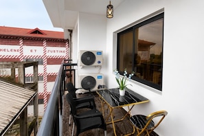 Uma varanda com duas unidades de ar condicionado, uma mesa com cadeiras e uma janela com vista para edifícios.