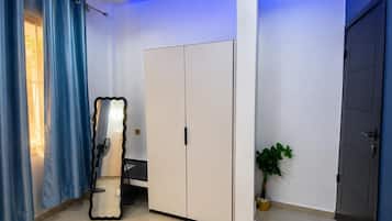 A room with a wardrobe, a mirror, a potted plant, and a door.