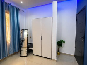 Una habitación con armario, espejo, planta en maceta y una puerta.