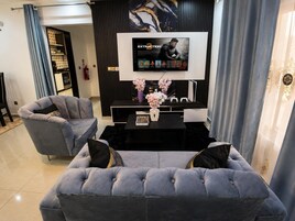 Una sala de estar moderna con un sofá gris, una mesa de centro negra y un televisor de pantalla plana montado en una pared negra.