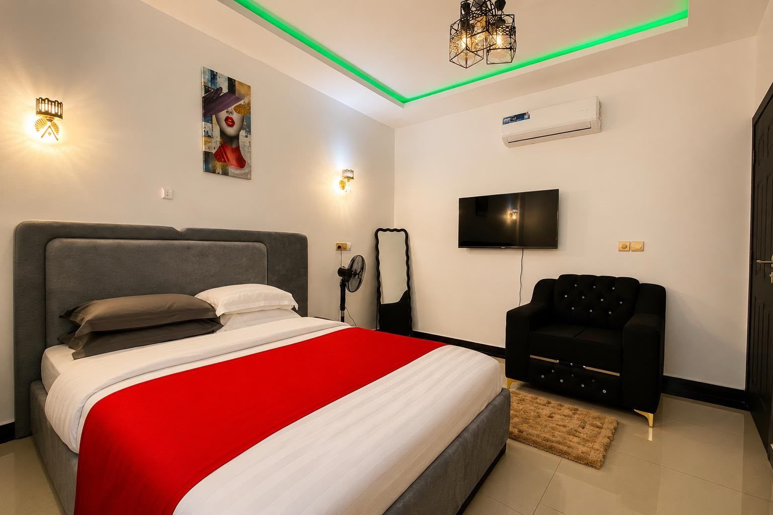 A modern bedroom with a bed, a black armchair, a TV, and a ceiling light fixture.