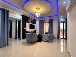 A modern living room with a flat-screen TV, a tufted sofa, and a coffee table. - Nova vista home (Douala)