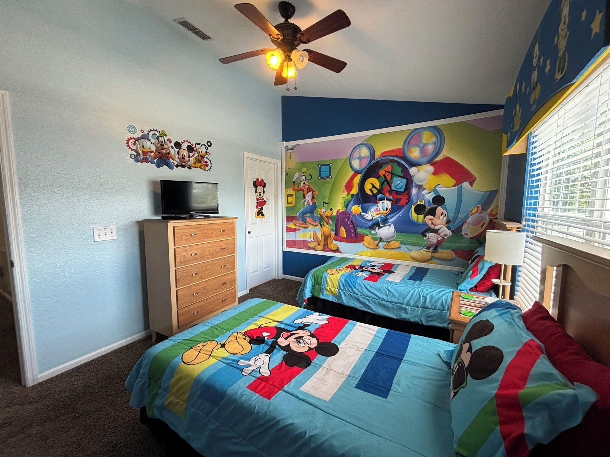Ein Schlafzimmer mit zwei Betten, einem Deckenventilator, einem Fernseher und einem Wandbild.