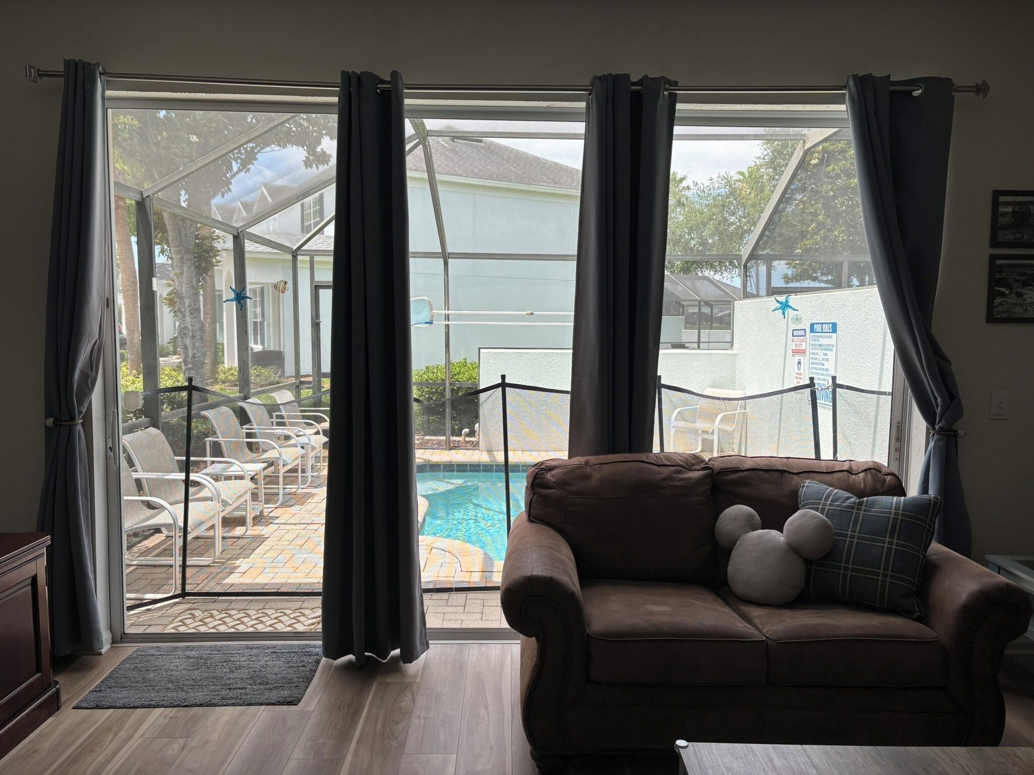 Una sala de estar con un sofá marrón, vista a la piscina y puerta de cristal que da al exterior.