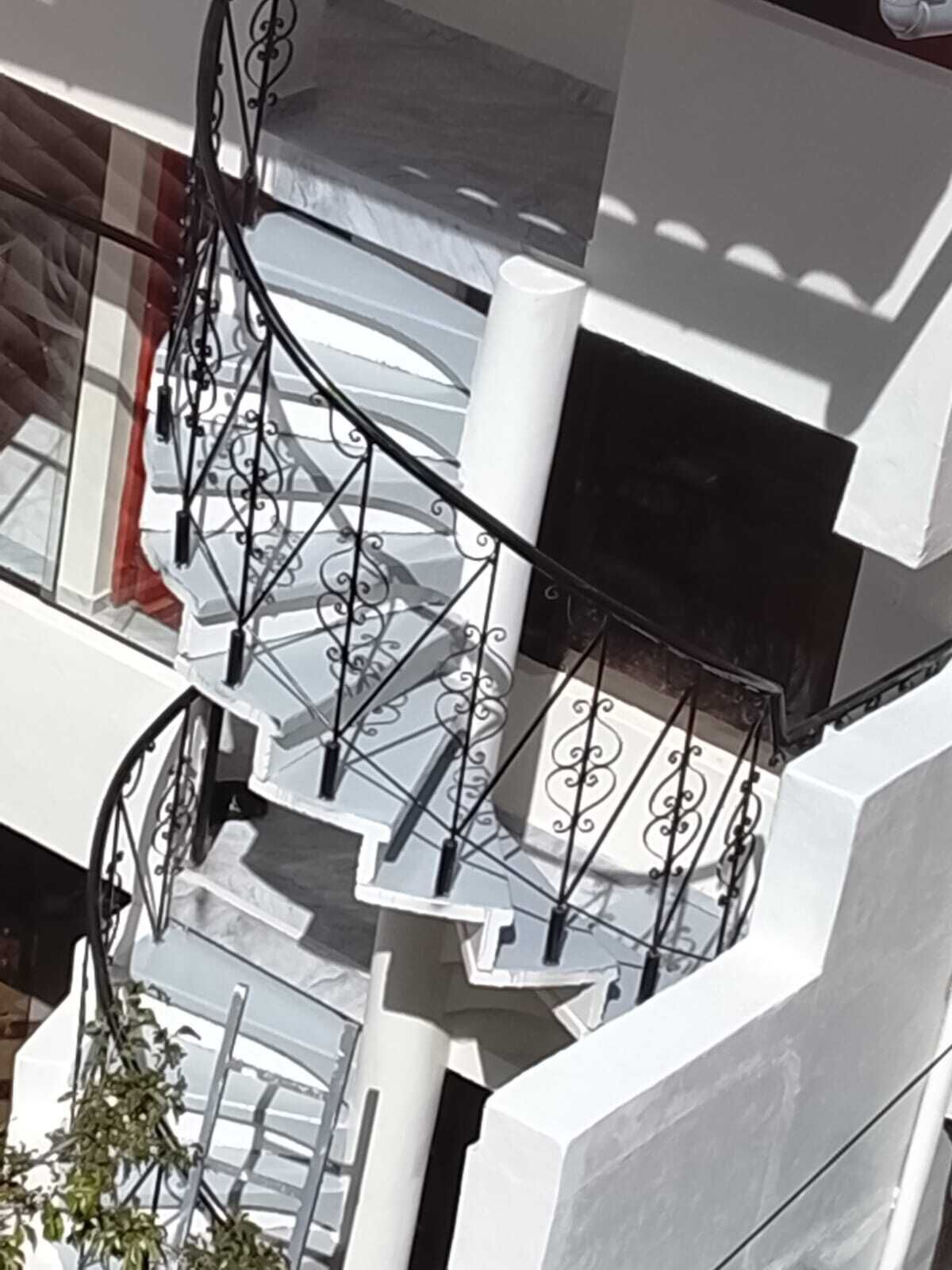 Un escalier en colimaçon avec une rampe en métal, des murs blancs et une colonne.