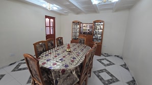 A dining room with a round table, wooden chairs, a floral tablecloth, a cabinet with glass doors, and a ceiling fan. - Terrific 5-bedroom house in charming Cusco for your getaway (Cusco)
