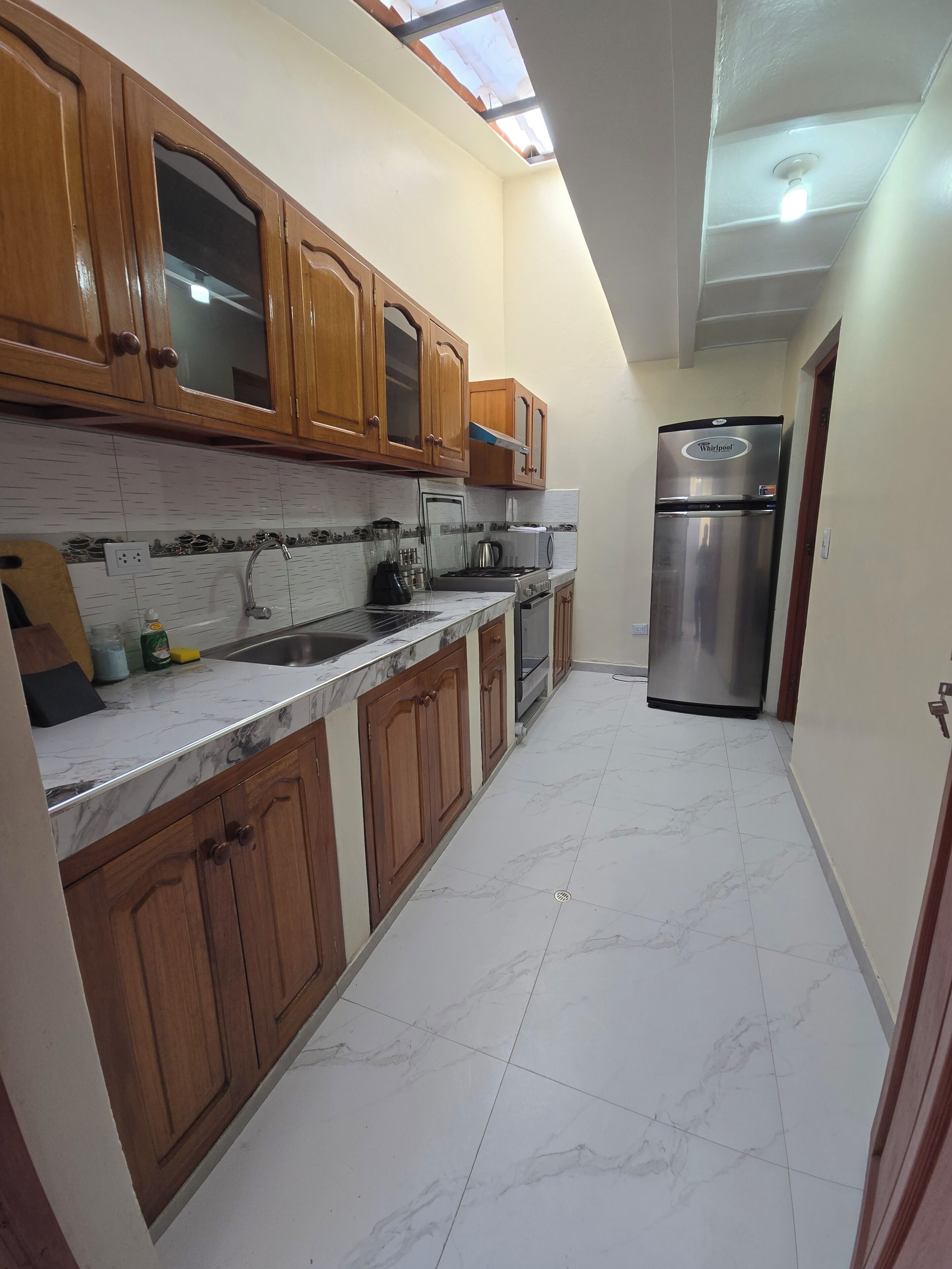 A kitchen with wooden cabinets, a stainless steel refrigerator, and a tiled floor.