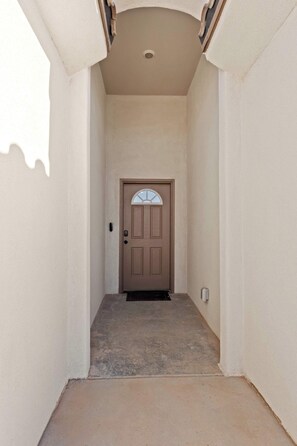 A narrow hallway with a brown door at the end, a small step leading up to it, and a light switch on the wall to the right.