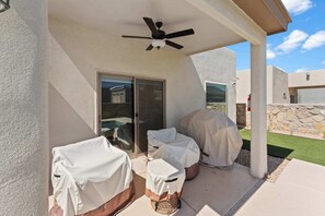 An outdoor covered patio area with a ceiling fan, covered seating, and a view of a pool and house in the background.
